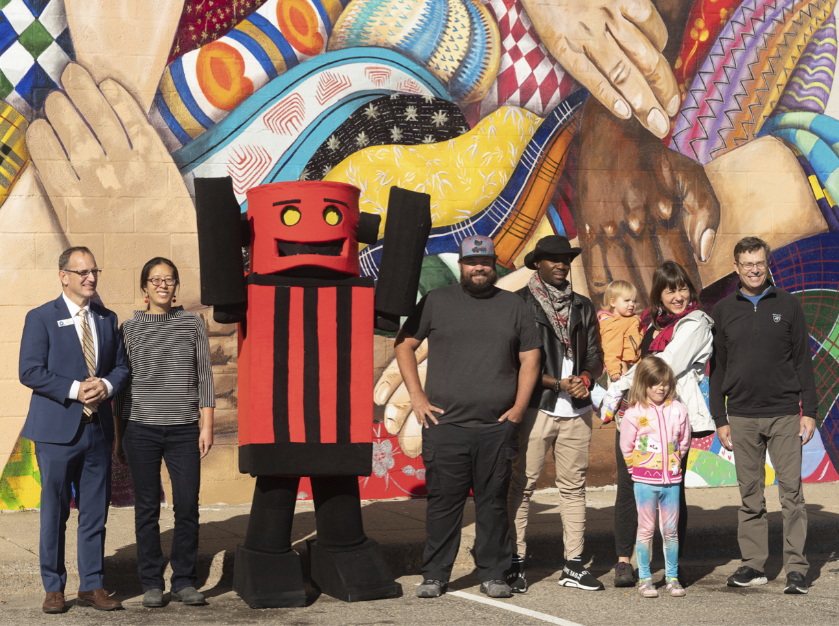<p>(l to r) Mayor of Crystal, MN, Jim Adams; Springboard for the Arts Director of Community Development Programs Jun-Li Wang; Artists Nick Knutson (in the robot costume), Shawn McCann, and Geno Okok; Hennepin County Senior Planning Analyst Crystal Myslajek and family; Hennepin County Commissioner Mike Opat (Dist. 1), at the Art on the Strip celebration in Crystal, in front of a new mural commissioned from McCann for Cultivate Bottineau.</p>
<p>	Photo Credit: Peter Jamus</p>
