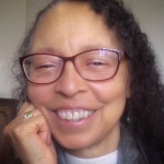 A smiling woman with dark curly hair and wearing red glasses 