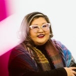 A smiling woman in cat-eye glasses and a colorful plaid scarf.