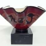 A dark red, fluted glass bowl with black and beige streaks going horizontally through the exterior center, sitting atop a black marble base