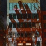 An image of a hand being projected upon a five-story building.