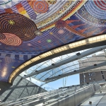 Mosaic art on a ceiling above escalators leading into a subway station.