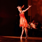A dancer in a flowy orange dress strikes a pose on a stage.