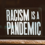 A photo of a sign in a window that reads "Racism is a pandemic"