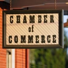 A sign that reads "Chamber of Commerce" hanging outside a building.