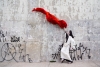 A dancer dressed in white waves a large red cloth in the air in front of a concrete wall adorned with spray painted graffiti written in Japanese characters.